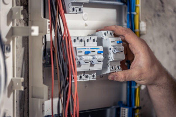 A male electrician works in a switchboard with an electrical connecting cable, connects the equipment with tools.